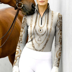 Model wearing the RIDER ATELIER Equestrian Chain & Medallion Print Riding Top at the stable, with a chestnut horse, highlighting the print’s warm sepia tones
