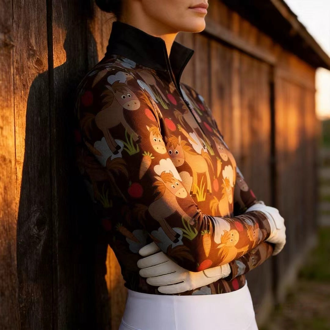 Woman wearing RIDER ATELIER cute cartoon horse dark brown quarter-zip top leaning on a barn at sunset