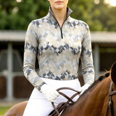 Woman wearing RIDER ATELIER diamond horse silhouette equestrian quarter-zip top in taupe gray, riding a chestnut horse at the equestrian stable
