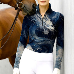 Woman wearing the RIDER ATELIER Deep Blue Chinese Dragon Print Long-Sleeve Quarter-Zip Riding Top leaning against a stable wall, with a chestnut horse nuzzling her shoulder, highlighting the print’s intricate scale details up close
