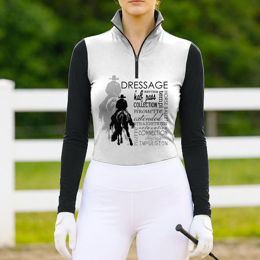 Woman wearing the RIDER ATELIER Black & White Dressage Word Cloud Print Long-Sleeve Quarter-Zip Riding Top at a sunlit pasture with a white fence, holding a riding crop, showing the print’s monochrome tones in natural daylight
