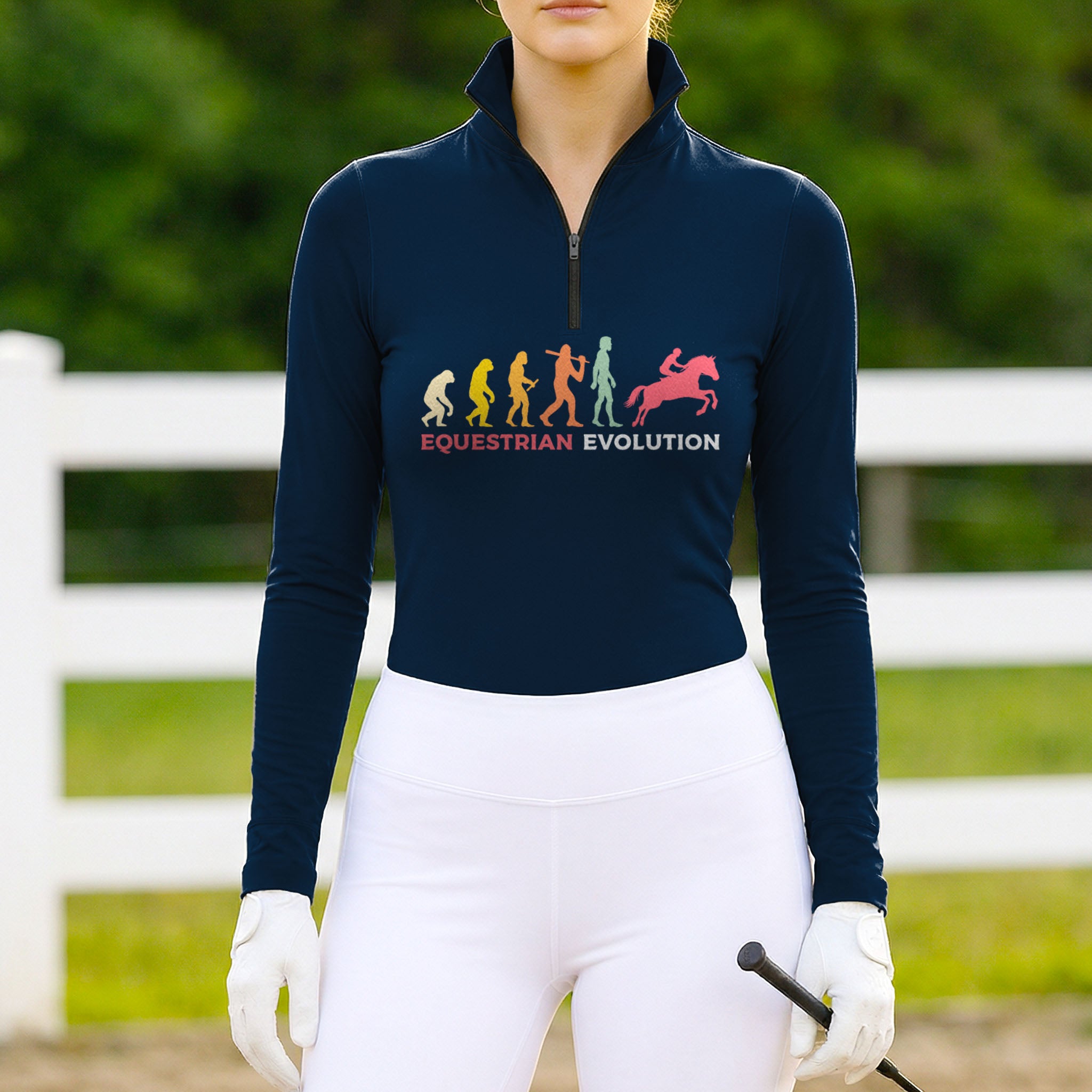 Model wearing the RIDER ATELIER Equestrian Evolution Graphic Print Long-Sleeve Riding Top at a sunlit pasture, holding a riding crop
