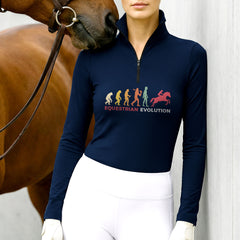 Model wearing the RIDER ATELIER Equestrian Evolution Graphic Print Long-Sleeve Riding Top at the stable, with a chestnut horse, highlighting the print’s colorful silhouettes

