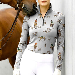 Woman wearing RIDER ATELIER fox hunt scene equestrian quarter-zip top in light gray at the barn with a chestnut horse