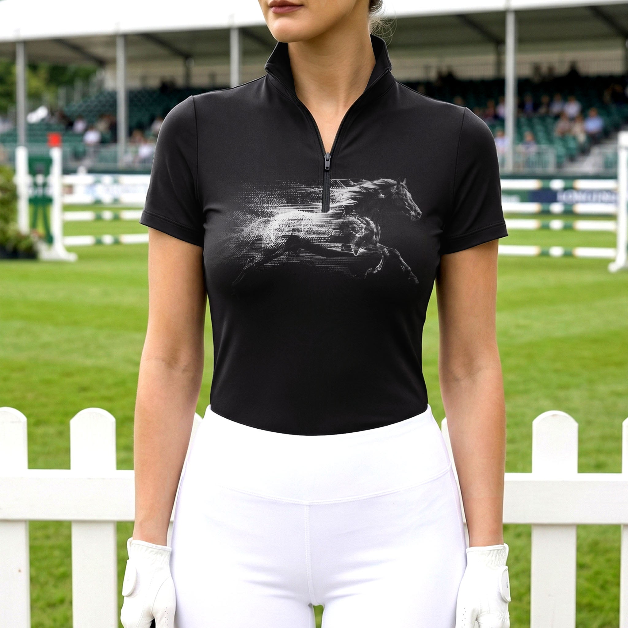 Model wearing the RIDER ATELIER Black Monochrome Galloping Horse Print Riding Top at an outdoor equestrian arena, with a white fence in the background
