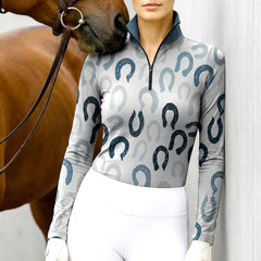Woman wearing RIDER ATELIER horseshoe print gray teal quarter-zip top with a chestnut horse