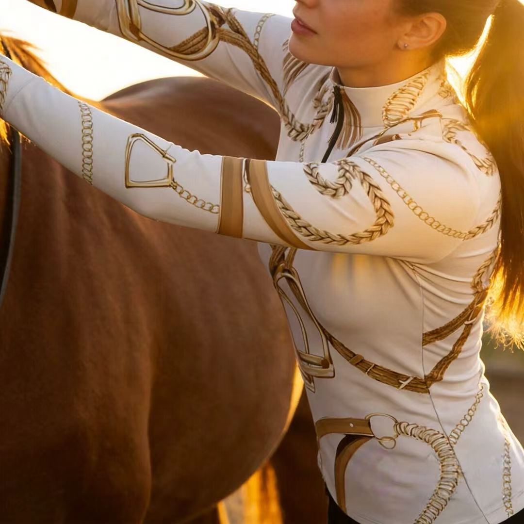 Model wearing the RIDER ATELIER Ivory Equestrian Tack Print Riding Tops at a sunset equestrian arena
