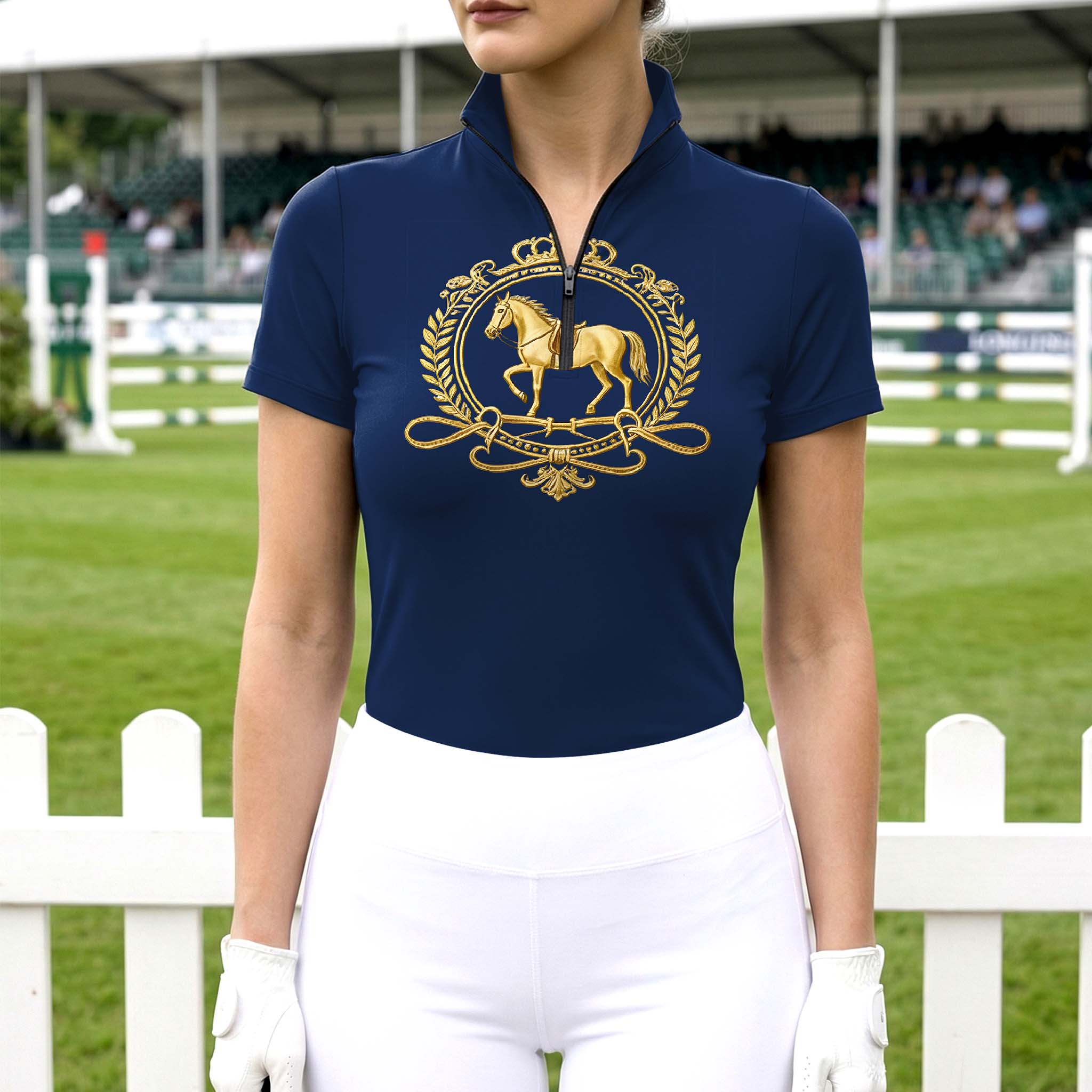 Model wearing the RIDER ATELIER Navy Gold Equestrian Crest Print Riding Top at an outdoor equestrian arena, with a white fence in the background

