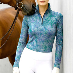 Woman wearing RIDER ATELIER tie-dye snaffle bit ocean blue-green quarter-zip top with a chestnut horse
