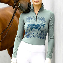 Woman wearing RIDER ATELIER Toile de Jouy horse sage green quarter-zip top with a chestnut horse