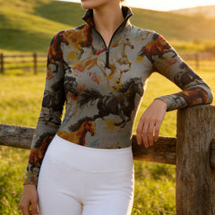 Woman wearing RIDER ATELIER watercolor galloping herd quarter-zip top leaning on a fence at sunset