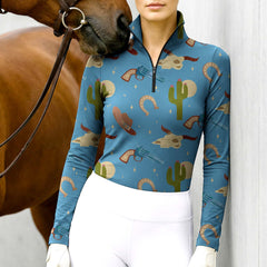 Model wearing the RIDER ATELIER Western Cowboy Print Riding Top at the stable, with a chestnut horse, highlighting the print’s playful details
