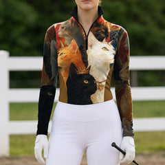Full-body model portrait wearing vintage regal cat print riding apparel beside white pasture fencing while gripping a riding crop
