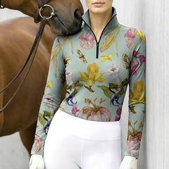 Full-body model shot wearing soft garden botanical equestrian long sleeve top at sunlit green pasture white wooden fence, holding riding crop
