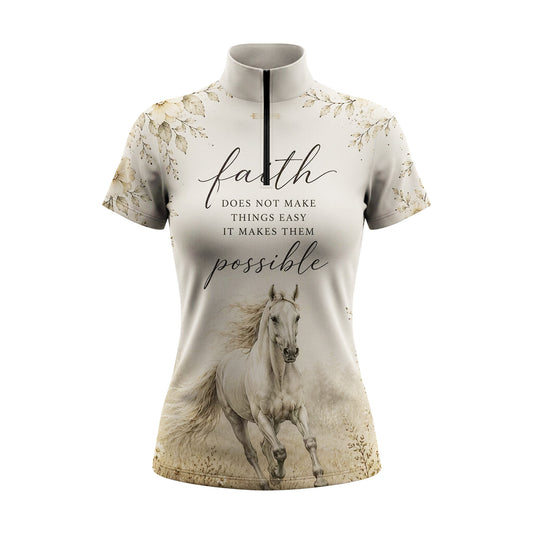 Full-body model shot wearing antique sepia spiritual wildflower horse print short sleeve riding top at outdoor equestrian show jumping arena with spectator stands, holding riding crop
