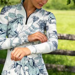 Outdoor green field lifestyle close‑up shot of female rider adjusting sleeve wearing off‑white sketch horse wild floral print long‑sleeve riding top