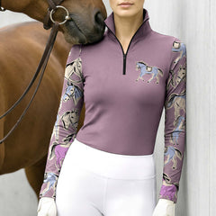 Model standing beside a chestnut horse against light grey stable wall wearing dusty mauve split pastel pony long sleeve riding top