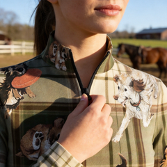 Warm sunlit countryside stable outdoor close-up shot focusing on stand collar, black half-zip and front tartan plaid multi-breed puppy dog graphic riding top