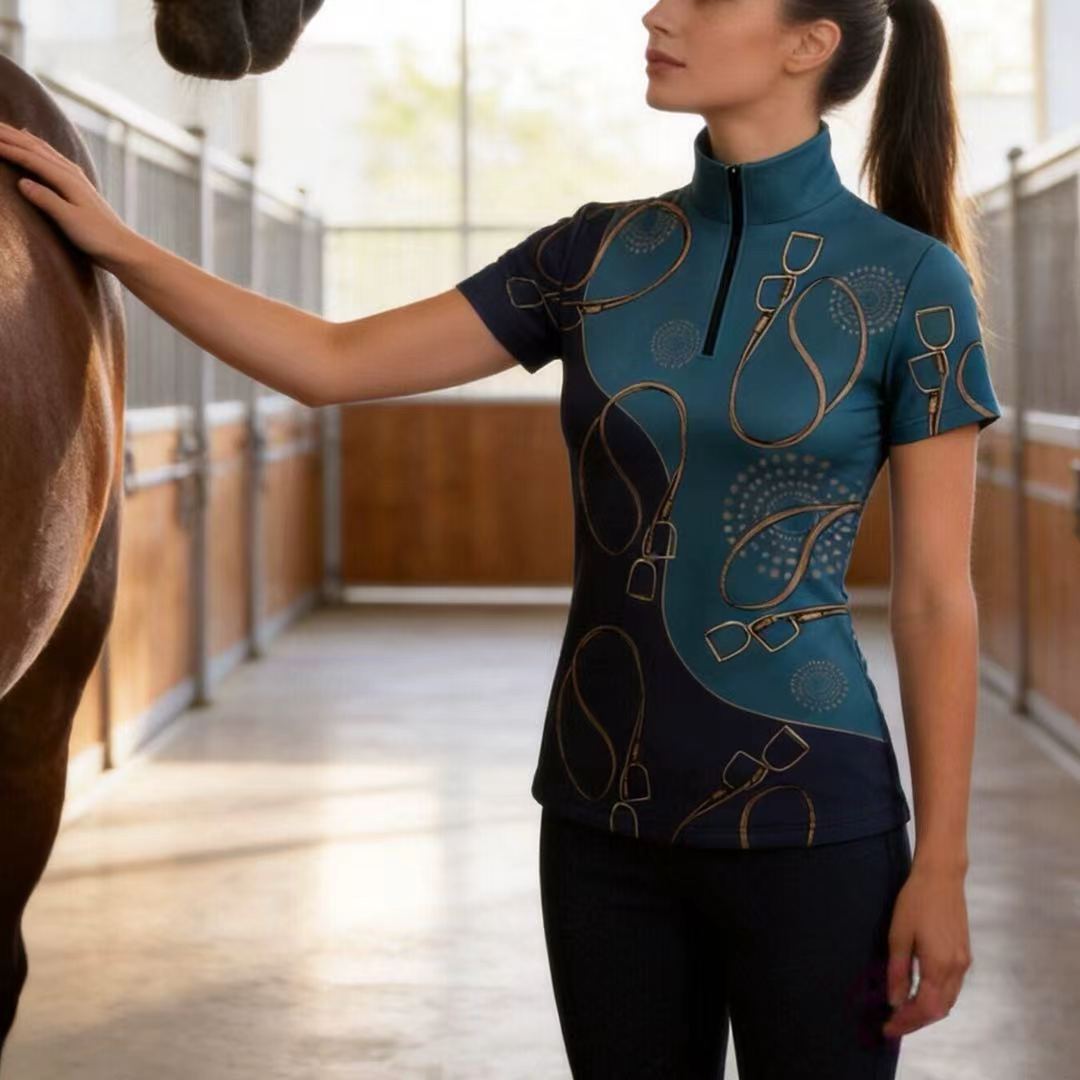 Model wearing teal & navy stirrup riding top touching a brown horse in the stable