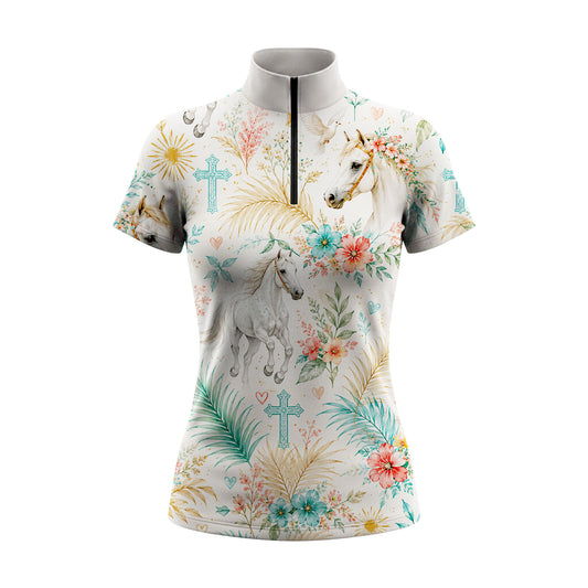 Full-body model shot wearing breezy tropical floral spiritual horse short sleeve top at outdoor equestrian show jumping arena with spectator stands, holding riding crop
