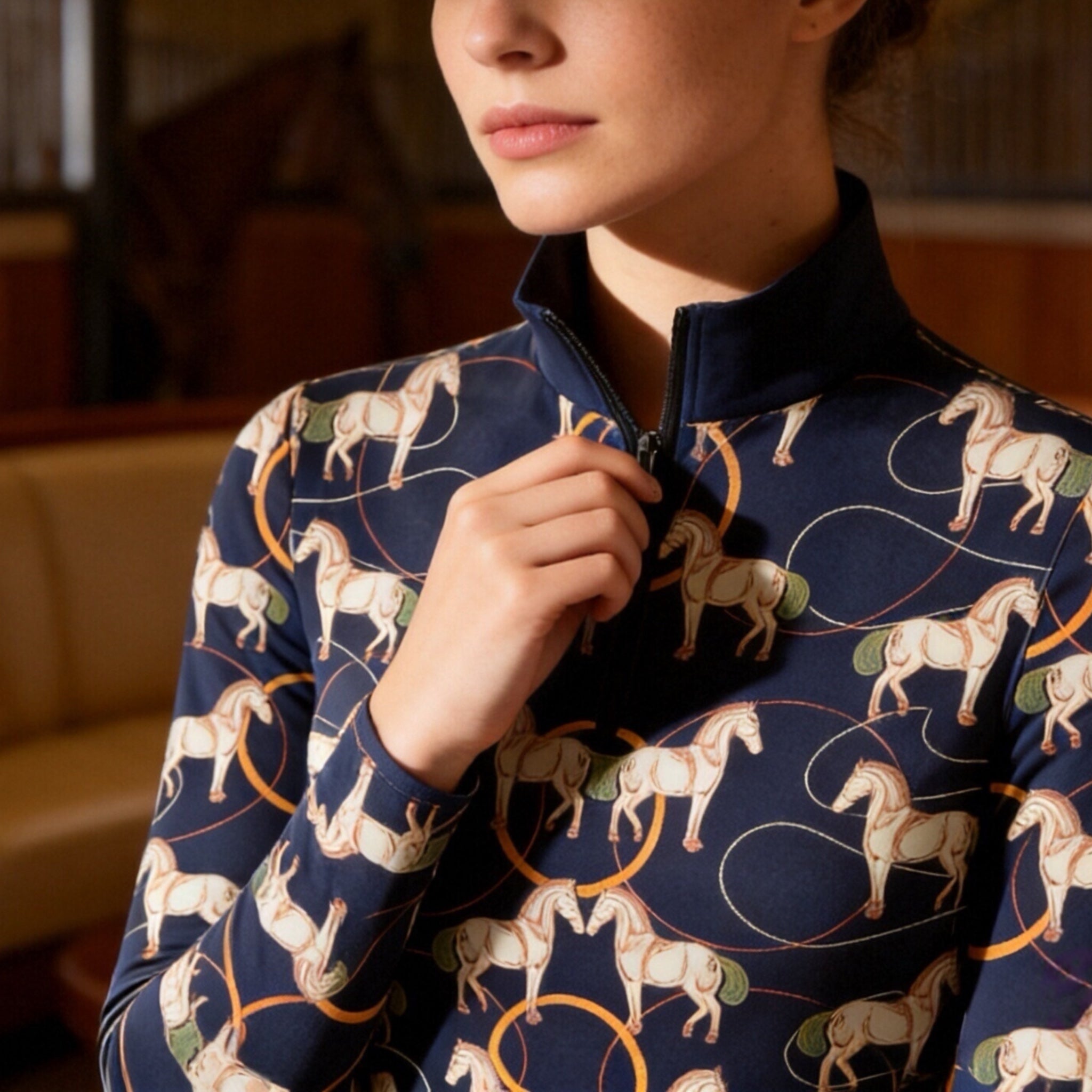 Close-up shot of model adjusting quarter-zip collar showcasing delicate line art horse and golden hoop print details on navy riding top