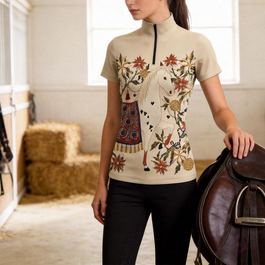 Warm sunlit wooden stable indoor shot of model standing beside brown leather saddle wearing soft cream beige short sleeve vintage spotted white horse floral heart tassel front print quarter-zip riding top
