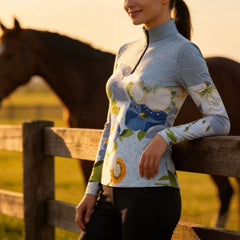 Model wearing the Watercolor Floral Print Long-Sleeve Riding Top at a sunset pasture, leaning on a wooden fence
