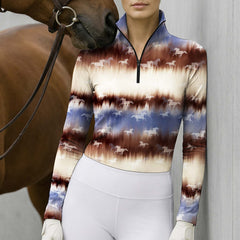 Model standing beside brown horse at light grey stable wall wearing warm brown-blue gradient tie-dye running horse long sleeve riding top
