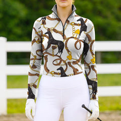 Full-body model shot wearing upscale heritage equestrian hardware long sleeve top at sunlit green pasture white wooden fence, holding riding crop
