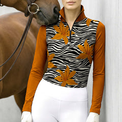 Model standing beside a horse resting against grey stable wall wearing zebra lily color-block long sleeve riding apparel
