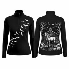 Barn fence lifestyle shot of two female equestrians, one showing back Halloween barn horse pumpkin print, other showing front bat silhouette on black long‑sleeve quarter‑zip riding top with white breeches and black riding gloves