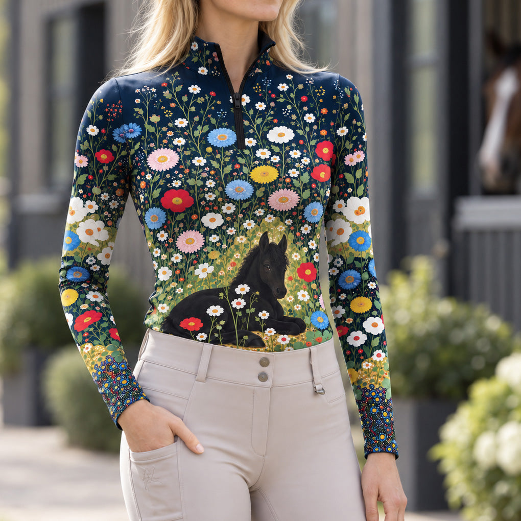Model wearing the navy floral foal print riding top with light breeches near a brown horse