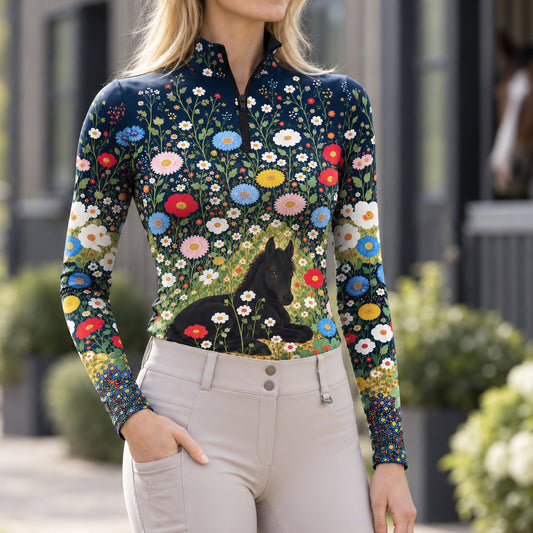 Model wearing the navy floral foal print riding top with light breeches near a brown horse