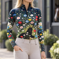 Model wearing the navy floral foal print riding top with light breeches near a brown horse