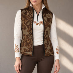 Woman wearing an open brown western horse and floral print quilted vest over a white quarter zip long sleeve top with brown riding breeches
