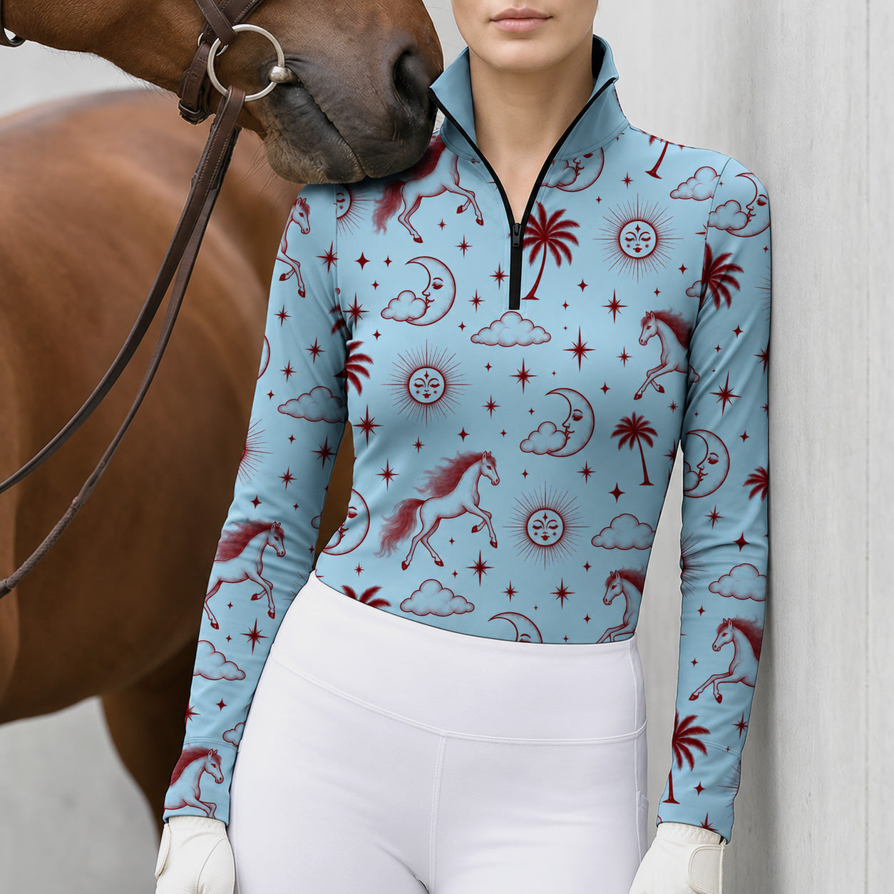 Woman in a light blue celestial horse print riding top with taupe breeches near a brown horse