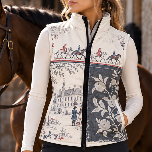 Woman wearing printed chateau equestrian vest over a white long sleeve top with black riding pants near horses