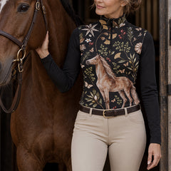 Woman wearing the black quarter zip riding top with a horse and botanical print while holding a riding crop