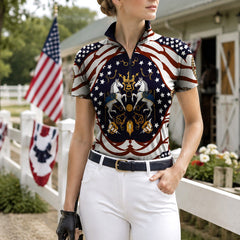 Farm lifestyle shot of female rider standing beside white wooden fence with american flag backdrop wearing flag‑inspired heraldic horse print riding top