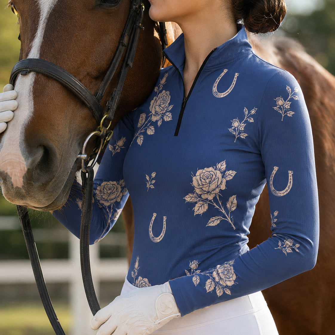 Close‑up lifestyle shot of female equestrian beside brown horse wearing navy floral horseshoe‑pattern long‑sleeve quarter‑zip riding top