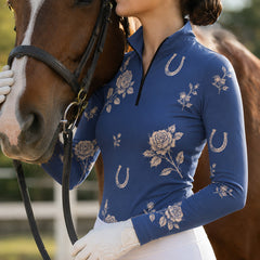Close‑up lifestyle shot of female equestrian beside brown horse wearing navy floral horseshoe‑pattern long‑sleeve quarter‑zip riding top