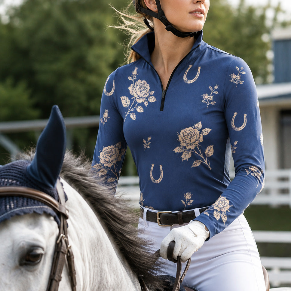 Rider mounted on grey horse inside equestrian arena wearing navy‑blue vintage rose horseshoe long‑sleeve performance riding top