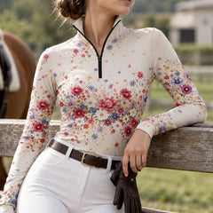 Cream floral print long sleeve quarter zip riding top worn with white breeches while standing near horses