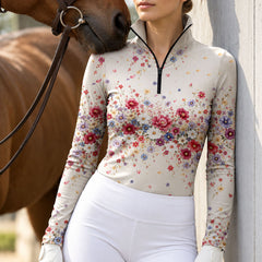 Cream floral print long sleeve quarter zip riding top paired with light grey breeches in an outdoor equestrian setting