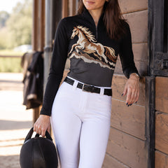 Woman wearing the black and dark gray galloping horse print riding top with white riding breeches and a riding helmet