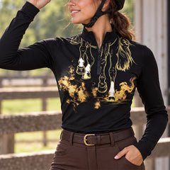 Woman wearing the black long sleeve quarter zip riding top with brown breeches and a black riding helmet near wooden fencing