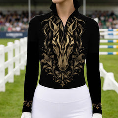 Model wearing black long sleeve quarter zip riding top with gold horse print and white breeches in a show jumping arena