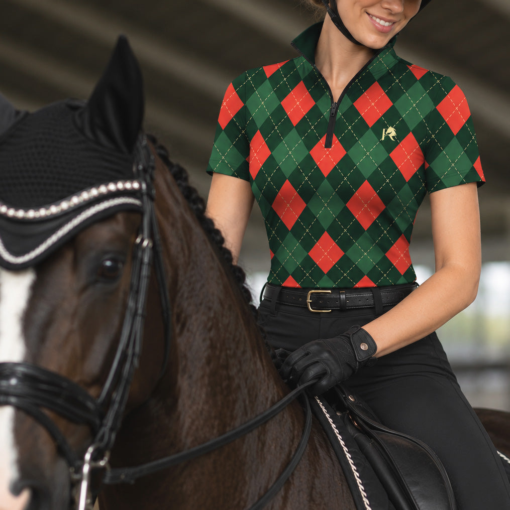 Rider wearing a green argyle short sleeve quarter zip riding top seated on a dark brown horse with a white facial blaze in an indoor covered riding arena