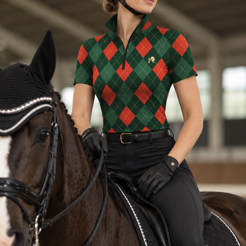 Rider wearing a green argyle short sleeve quarter zip riding top seated on a dark brown horse with a white facial blaze in an indoor covered riding arena