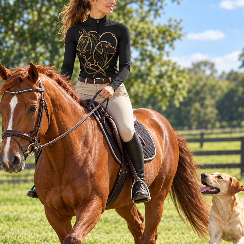 Woman wearing the black quarter zip riding top with light beige breeches while riding a chestnut horse in a grassy fenced field